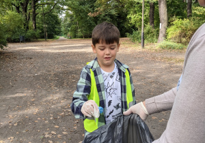 Na zdjęciu widać chłopca wyrzucającego do worka śmieci znalezione w parku podczas akcji "Sprzątanie świata"